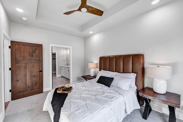 carpeted bedroom featuring a raised ceiling, connected bathroom, and ceiling fan