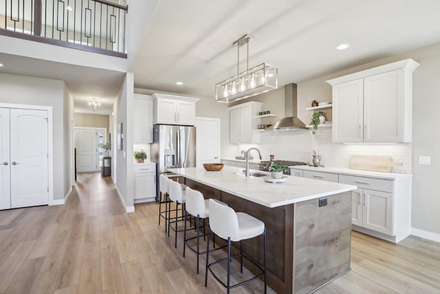 kitchen featuring open shelves, stainless steel fridge with ice dispenser, a kitchen bar, wall chimney exhaust hood, and backsplash