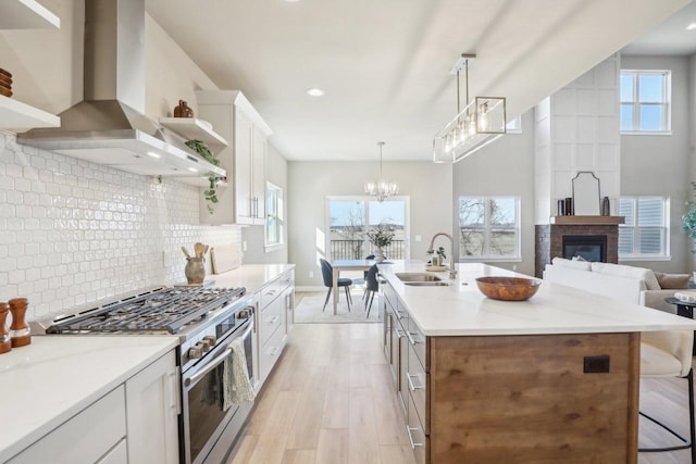 kitchen featuring stainless steel range with gas cooktop, a sink, white cabinetry, wall chimney exhaust hood, and light wood-type flooring