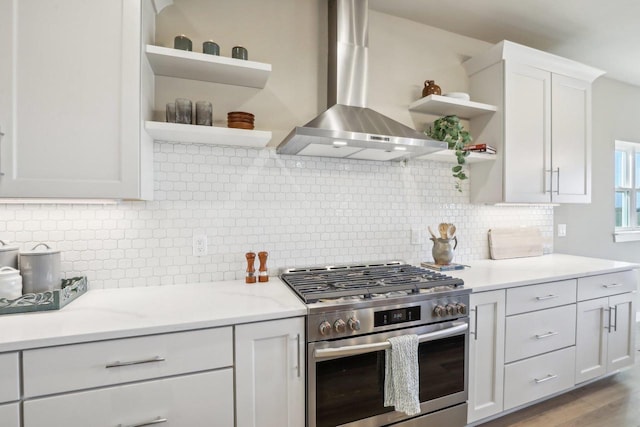 kitchen with open shelves, stainless steel range with gas stovetop, white cabinetry, wall chimney exhaust hood, and tasteful backsplash