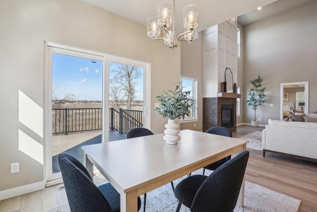 dining room featuring a notable chandelier, a high ceiling, a fireplace, light wood finished floors, and baseboards