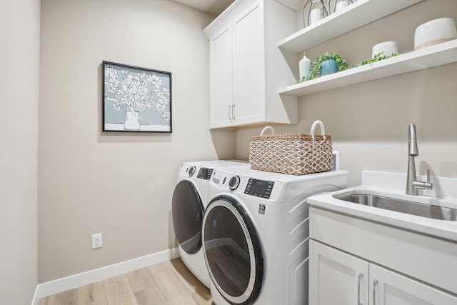 clothes washing area featuring baseboards, separate washer and dryer, cabinet space, a sink, and light wood-style floors