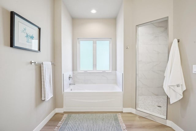 bathroom with a bath, a walk in shower, baseboards, and wood finished floors