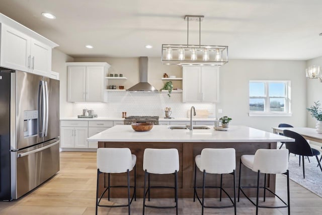 kitchen featuring a sink, open shelves, stainless steel fridge, wall chimney exhaust hood, and stove