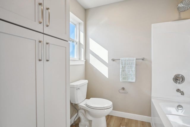 bathroom featuring tub / shower combination, toilet, baseboards, and wood finished floors