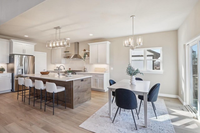 kitchen featuring light countertops, decorative backsplash, stainless steel refrigerator with ice dispenser, wall chimney exhaust hood, and open shelves