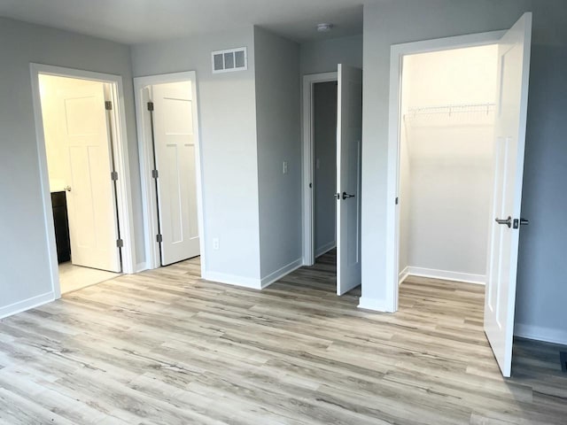 unfurnished bedroom featuring a walk in closet, light hardwood / wood-style floors, a closet, and ensuite bathroom