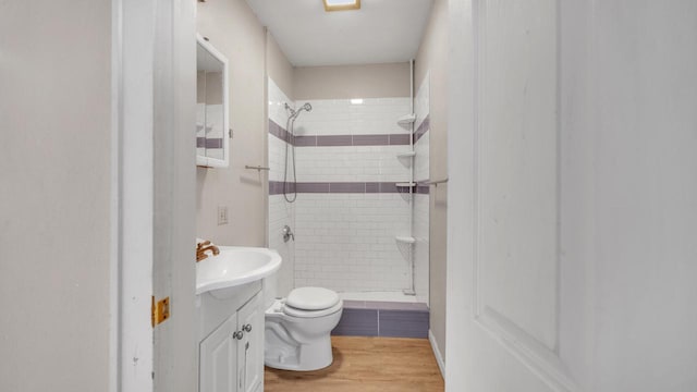 bathroom with a tile shower, hardwood / wood-style floors, vanity, and toilet