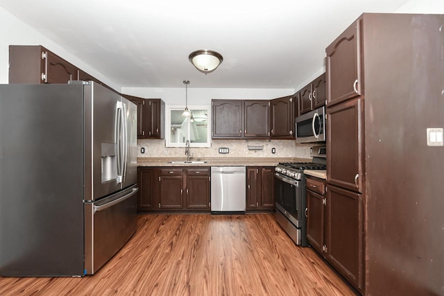 kitchen with sink, appliances with stainless steel finishes, dark brown cabinetry, light hardwood / wood-style floors, and decorative light fixtures