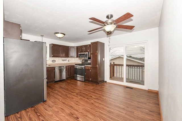 kitchen featuring dark wood-type flooring, ceiling fan, appliances with stainless steel finishes, dark brown cabinets, and decorative backsplash