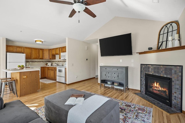 living room featuring light hardwood / wood-style floors, vaulted ceiling, a tiled fireplace, and ceiling fan