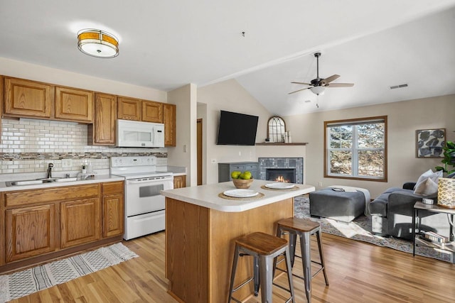 kitchen featuring white appliances, light hardwood / wood-style flooring, sink, a kitchen island, and a breakfast bar area