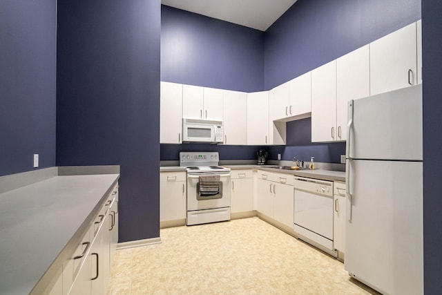 kitchen with sink, white appliances, white cabinets, and a towering ceiling