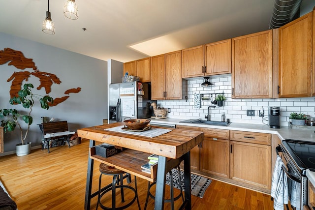 kitchen featuring pendant lighting, sink, appliances with stainless steel finishes, light hardwood / wood-style floors, and decorative backsplash