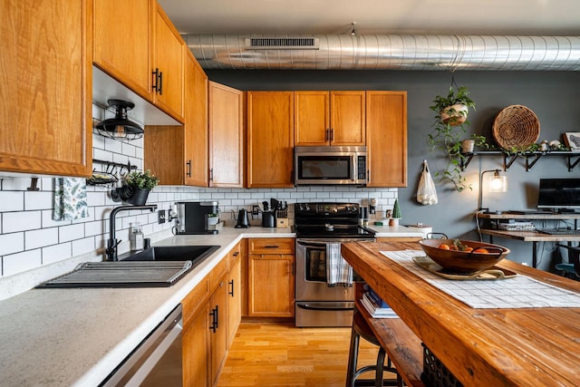 kitchen with appliances with stainless steel finishes, sink, backsplash, and light wood-type flooring