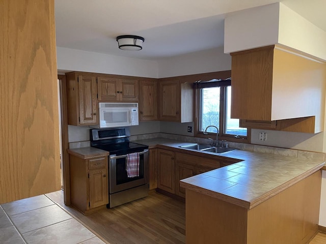 kitchen with sink, light hardwood / wood-style flooring, tile counters, stainless steel electric range oven, and kitchen peninsula