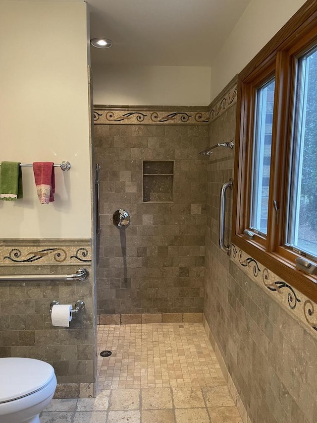 bathroom with a tile shower, toilet, and tile walls