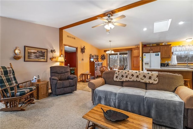 carpeted living room with ceiling fan with notable chandelier, vaulted ceiling with skylight, and sink