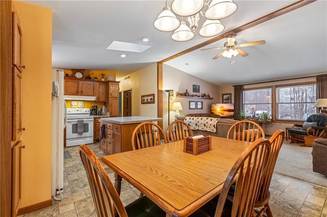 dining area featuring ceiling fan with notable chandelier and vaulted ceiling with skylight