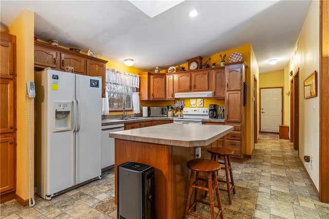 kitchen with sink, a kitchen island, stainless steel appliances, vaulted ceiling with skylight, and a kitchen bar