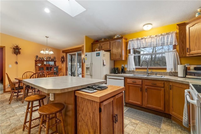 kitchen featuring sink, hanging light fixtures, a kitchen breakfast bar, a kitchen island, and white appliances