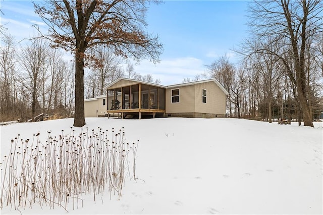 snow covered back of property featuring a sunroom