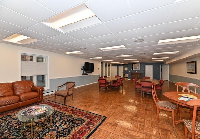 living room with parquet floors, a baseboard radiator, and a drop ceiling