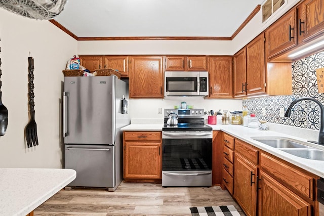 kitchen with ornamental molding, stainless steel appliances, sink, and light wood-type flooring