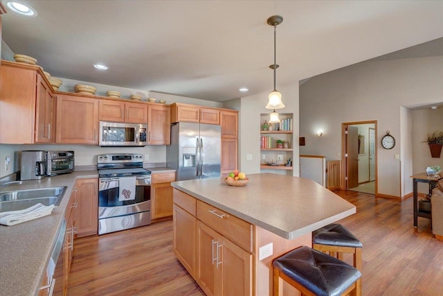 kitchen featuring appliances with stainless steel finishes, decorative light fixtures, sink, a center island, and light hardwood / wood-style floors