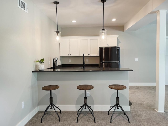 kitchen with hanging light fixtures, sink, white cabinets, and stainless steel refrigerator