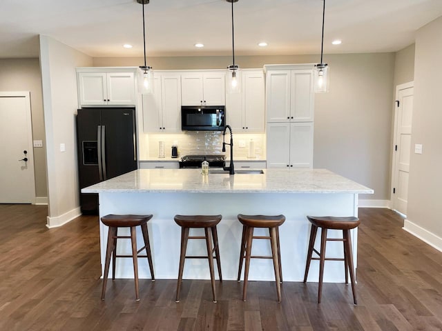 kitchen featuring light stone counters, black appliances, hanging light fixtures, an island with sink, and white cabinets