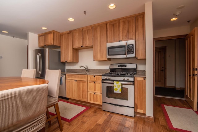 kitchen with light stone counters, sink, stainless steel appliances, and light hardwood / wood-style floors