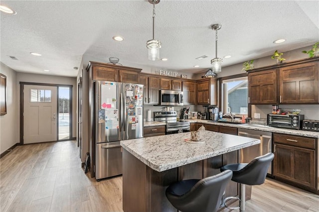 kitchen featuring a kitchen island, appliances with stainless steel finishes, pendant lighting, and light hardwood / wood-style floors