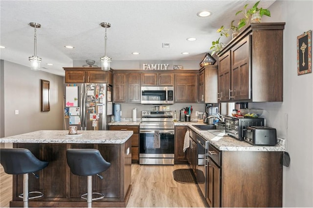 kitchen with sink, decorative light fixtures, a center island, light hardwood / wood-style flooring, and stainless steel appliances