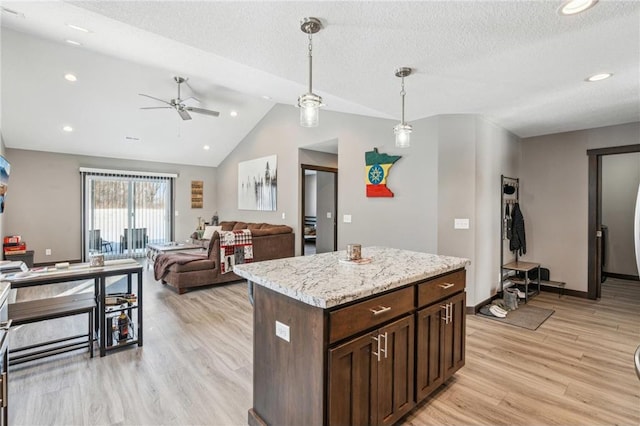 kitchen featuring pendant lighting, a center island, light stone counters, vaulted ceiling, and light wood-type flooring