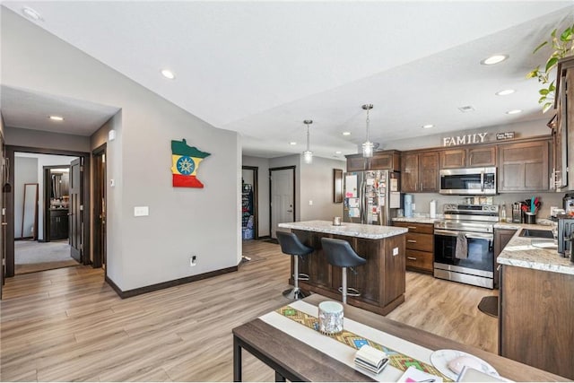 kitchen with appliances with stainless steel finishes, decorative light fixtures, a center island, light stone counters, and light hardwood / wood-style floors