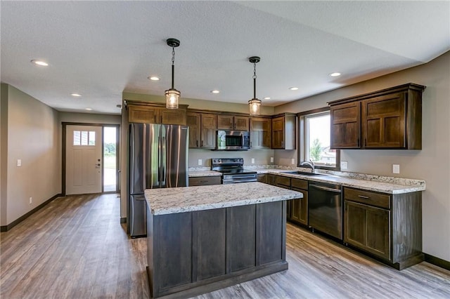 kitchen with sink, hanging light fixtures, appliances with stainless steel finishes, a kitchen island, and light stone countertops