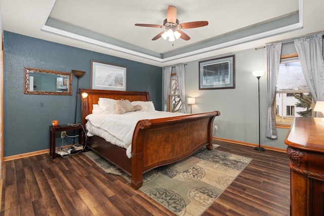 bedroom with a tray ceiling, dark wood-type flooring, and ceiling fan