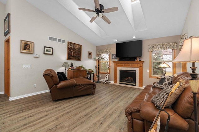 living room featuring ceiling fan, hardwood / wood-style floors, a skylight, high vaulted ceiling, and a tiled fireplace