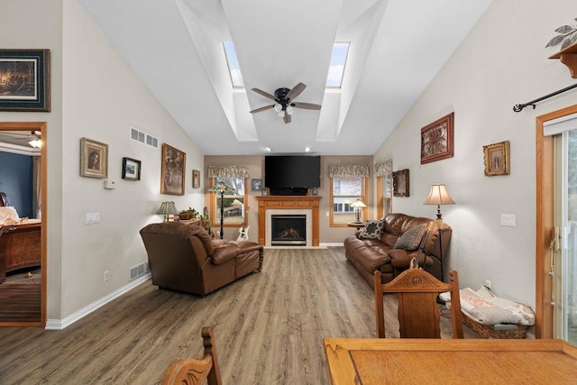 living room with a skylight, high vaulted ceiling, hardwood / wood-style flooring, ceiling fan, and a fireplace