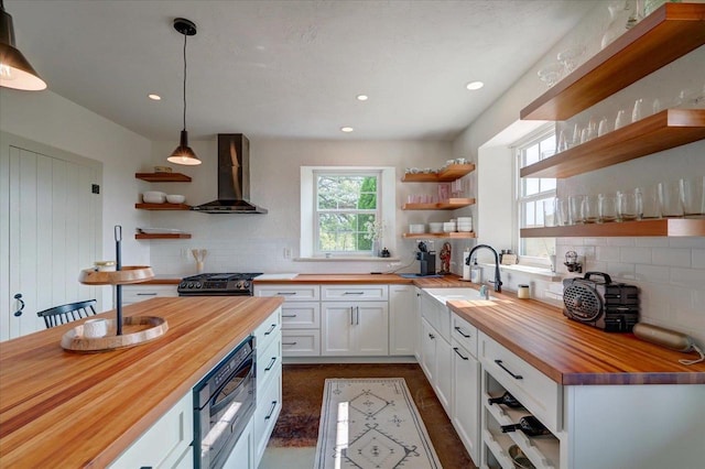 kitchen with sink, white cabinetry, wood counters, decorative light fixtures, and wall chimney exhaust hood