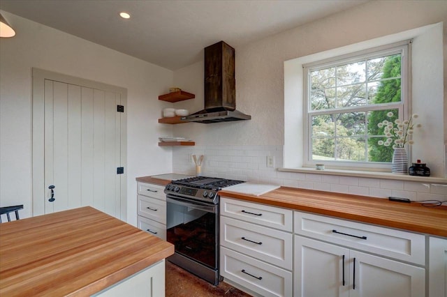 kitchen featuring wall chimney exhaust hood, butcher block counters, gas range, tasteful backsplash, and white cabinets