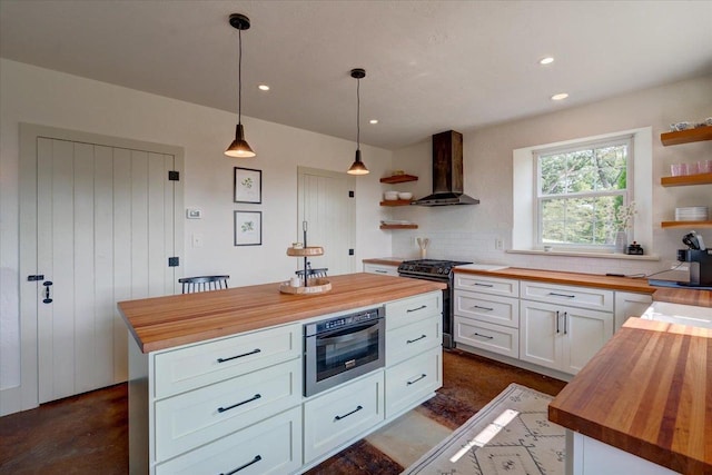 kitchen featuring wall chimney range hood, wooden counters, stainless steel gas stove, white cabinets, and a kitchen island