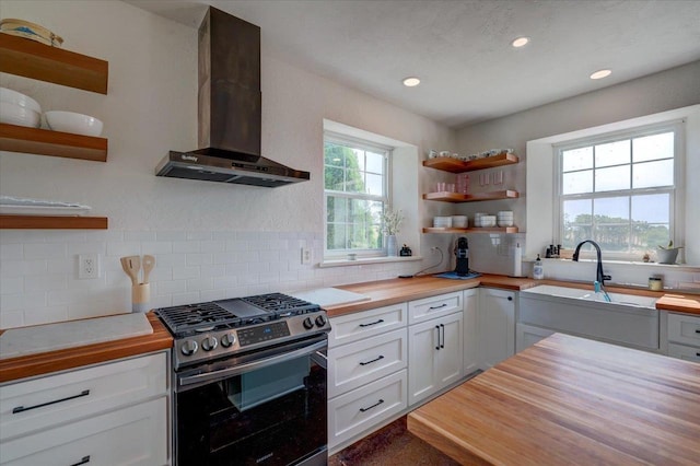 kitchen with white cabinets, wall chimney exhaust hood, butcher block countertops, and stainless steel gas range oven