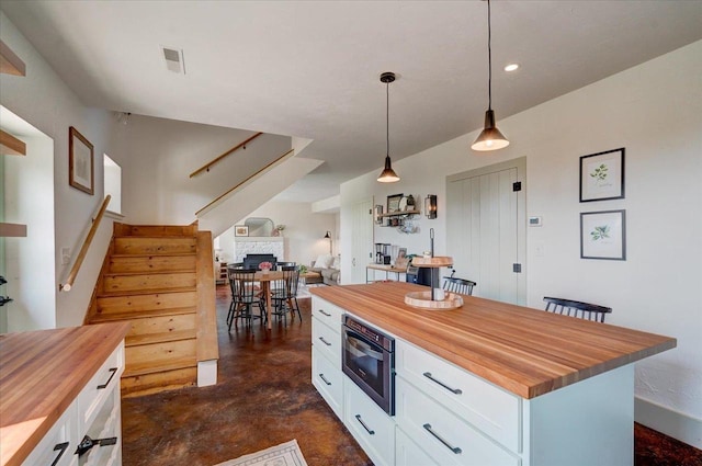 kitchen with pendant lighting, butcher block countertops, a kitchen island, and white cabinets