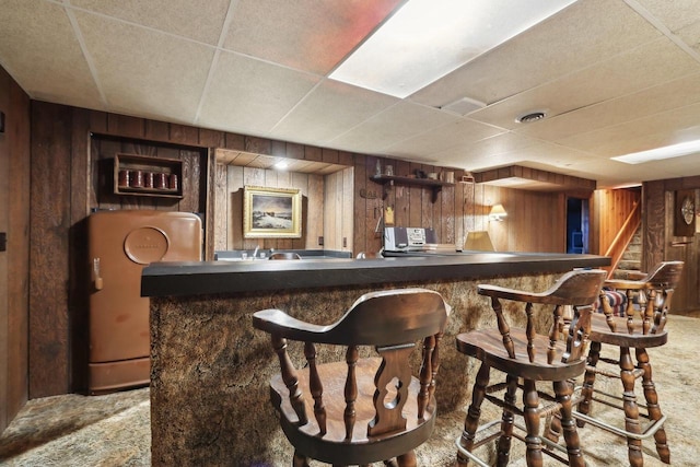 bar with carpet floors, a paneled ceiling, and wood walls