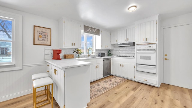 kitchen with a breakfast bar, dishwasher, white cabinets, kitchen peninsula, and white oven