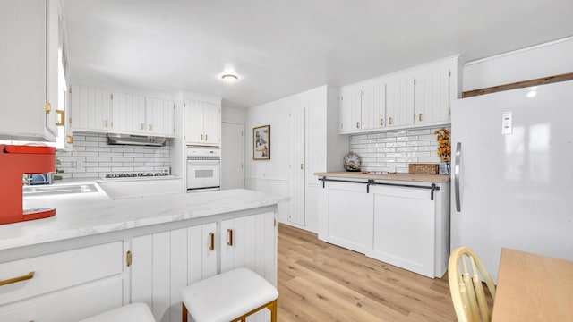 kitchen featuring white cabinetry, decorative backsplash, white appliances, and light hardwood / wood-style floors