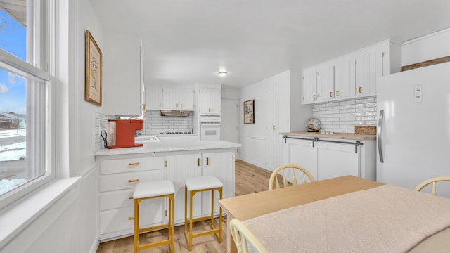 kitchen featuring white cabinetry, white appliances, light hardwood / wood-style floors, and decorative backsplash