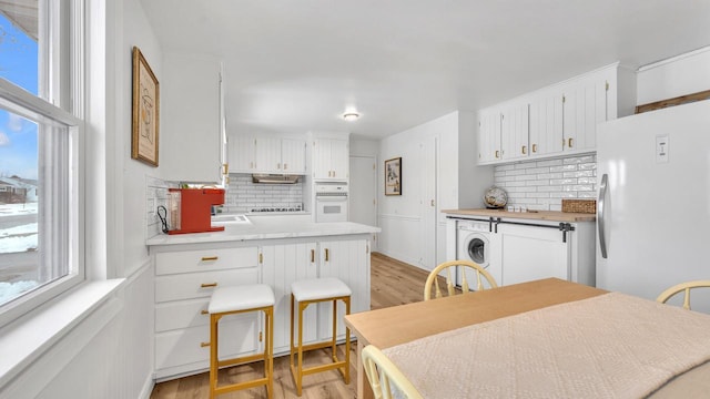 kitchen with white appliances, light hardwood / wood-style flooring, backsplash, white cabinets, and washer / clothes dryer